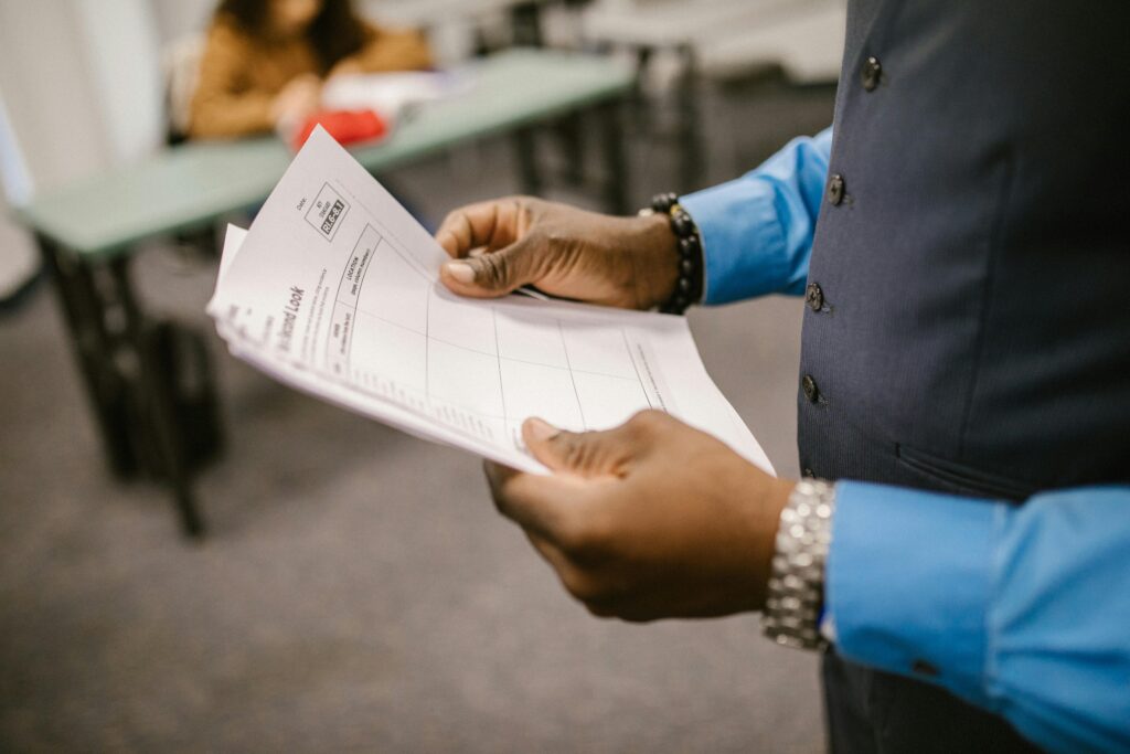 An instructor examining test papers in a classroom setting, focusing on education and evaluation.